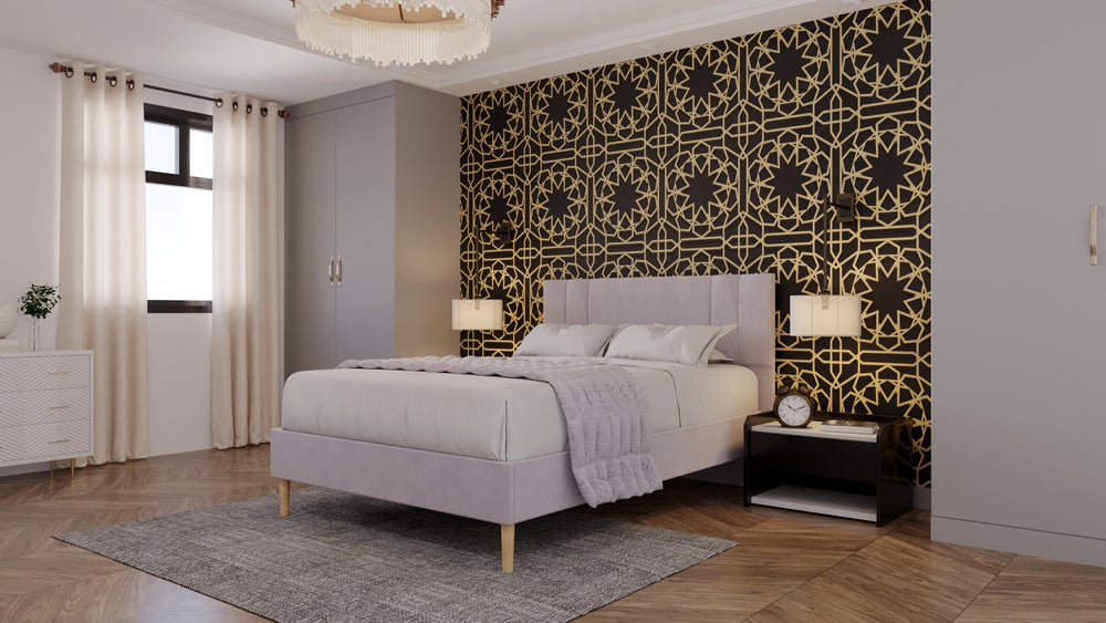 A bed in the middle of a room which has a feature wall of black and gold intricate wallpaper. The bed frame is a dusty pink, with a matching throw over the bed itself. Modern lights hang either side of the bed. 