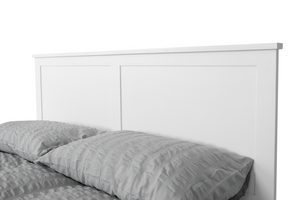 
                  
                    A close-up of a white, wooden bed frame with grey textured pillows. 
                  
                