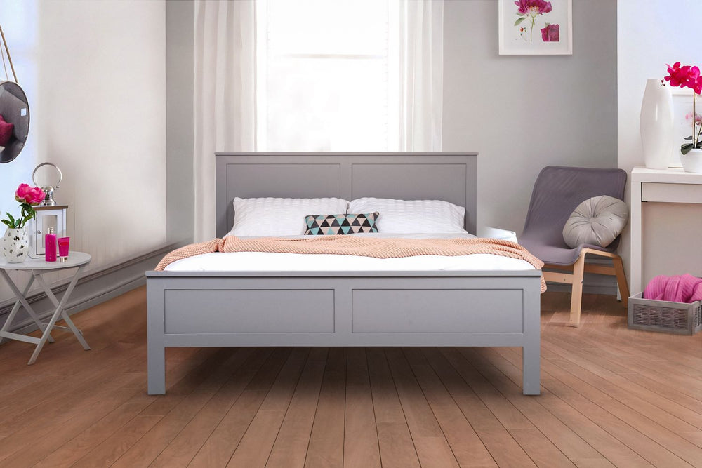 A white, wooden bed frame in a modern room with gray walls and a wooden floor. There are accents of pink in the room.